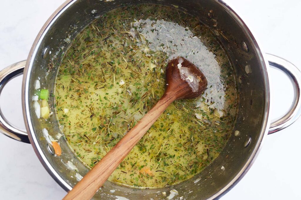 Broth added to a soup pot of vegetables and spices.