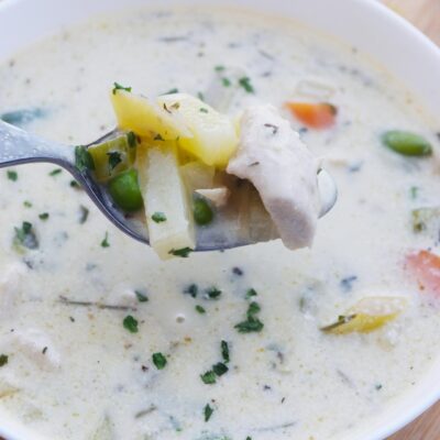 A spoon lifts some Chicken Pot Pie Soup out of a bowl full of this soup.