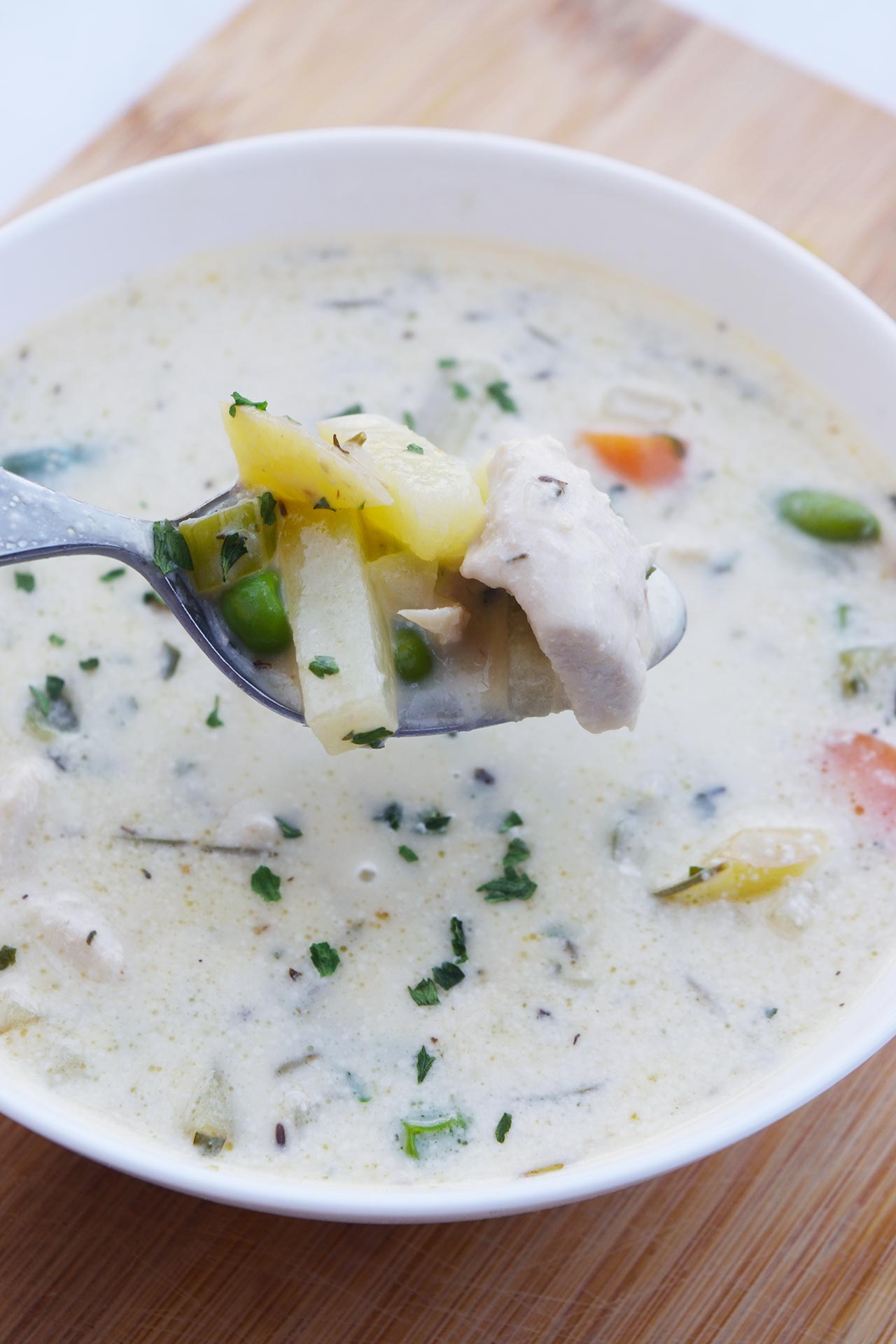 A spoon lifts some Chicken Pot Pie Soup out of a bowl full of this soup.