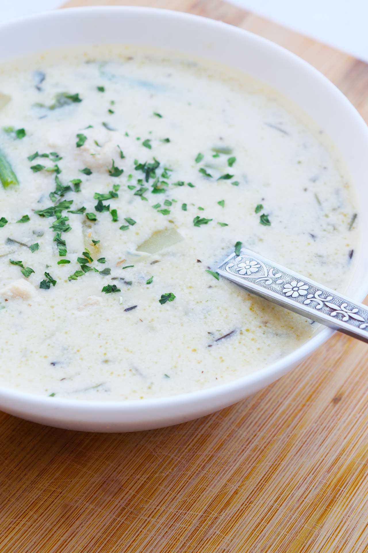 Side view of a bowl full of Chicken Pot Pie Soup sitting on a wood cutting board.