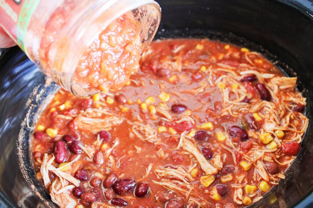 Adding salsa to the Chicken Taco Chili in a slow cooker.