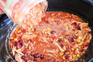 Adding salsa to the Chicken Taco Chili in a slow cooker.