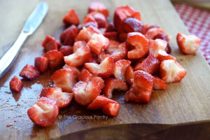 Quartered strawberries on a wood cutting board.