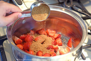 Adding sweetener to a pot of quartered strawberries.
