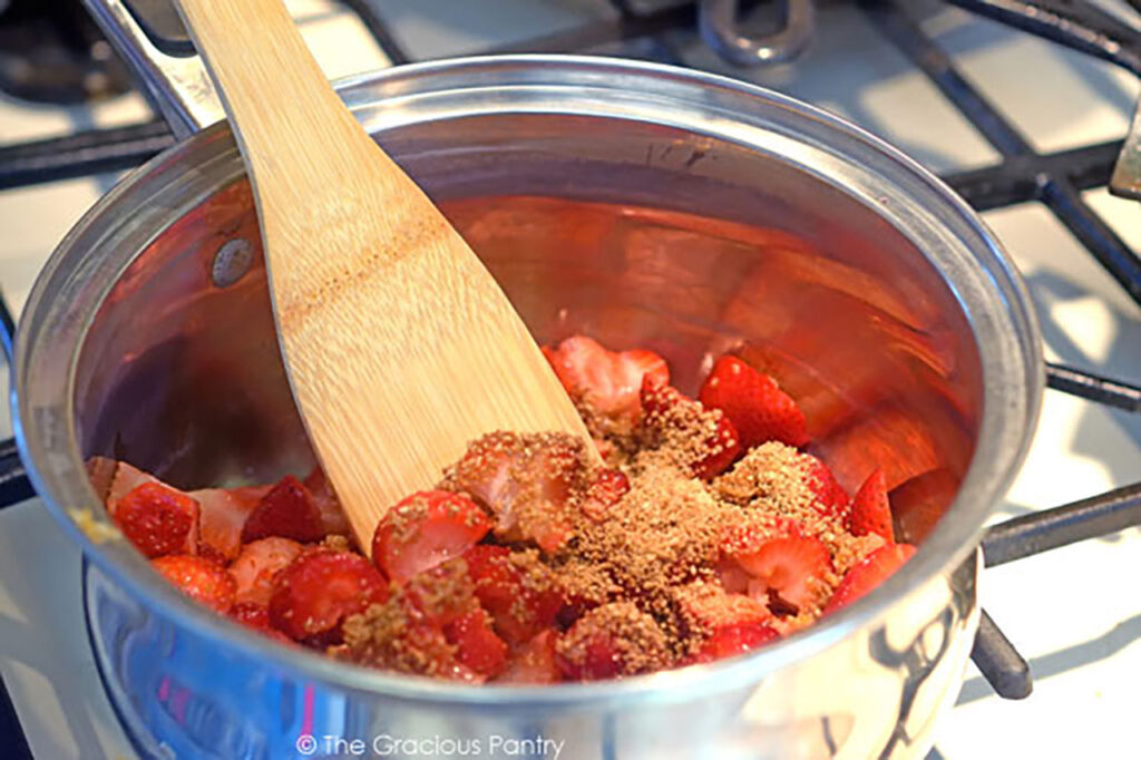 Stirring strawberries and sweetener together in a pot.