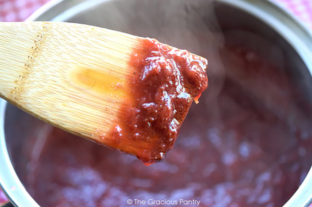 Showing finished Chunky Strawberry Pancake Syrup on a wooden spoon.
