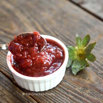 A spoon lifts some Chunky Strawberry Pancake Syrup from a small, white ramekin.