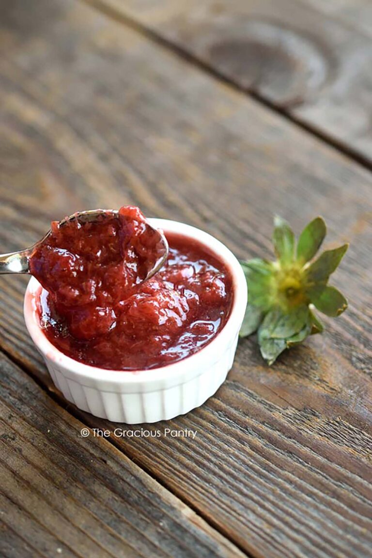 A spoon lifts some Chunky Strawberry Pancake Syrup from a small, white ramekin.