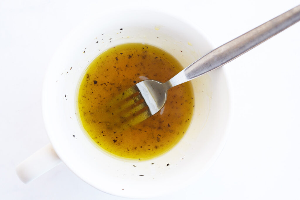 Dressing ingredients mixed with a fork in a white mug.