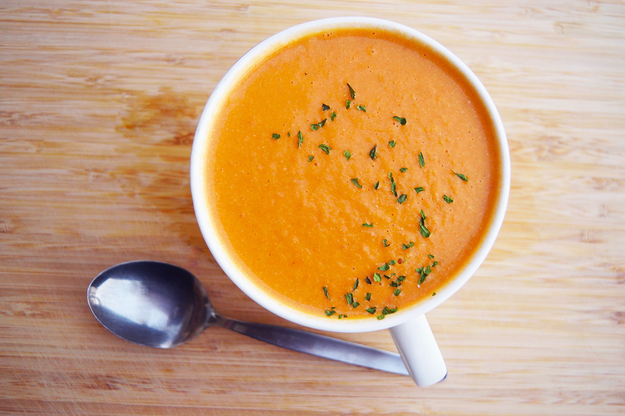 Overhead view of a white mug filled with creamy tomato soup.