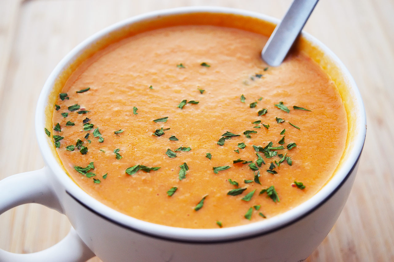 Side view of a white mug filled with creamy tomato soup.