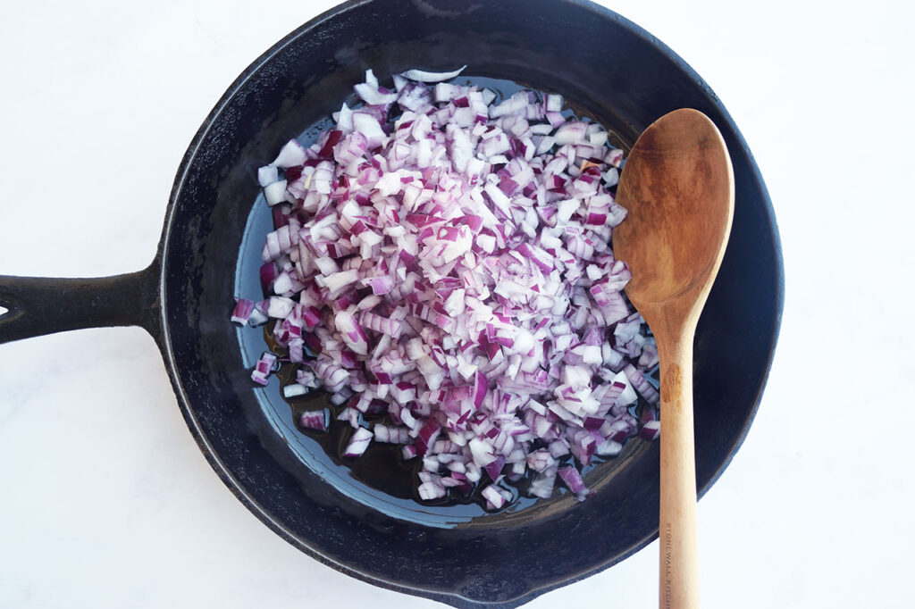 Chopped onions in a skillet with a wood spoon.