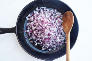 Chopped onions in a skillet with a wood spoon.