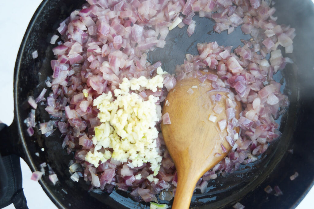 Minced garlic added to sautéed onions in a skillet.