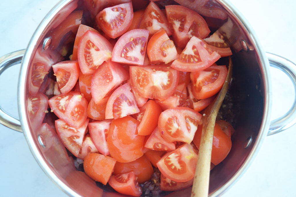 Fresh, quartered tomatoes added to onions and garlic in a soup pot.