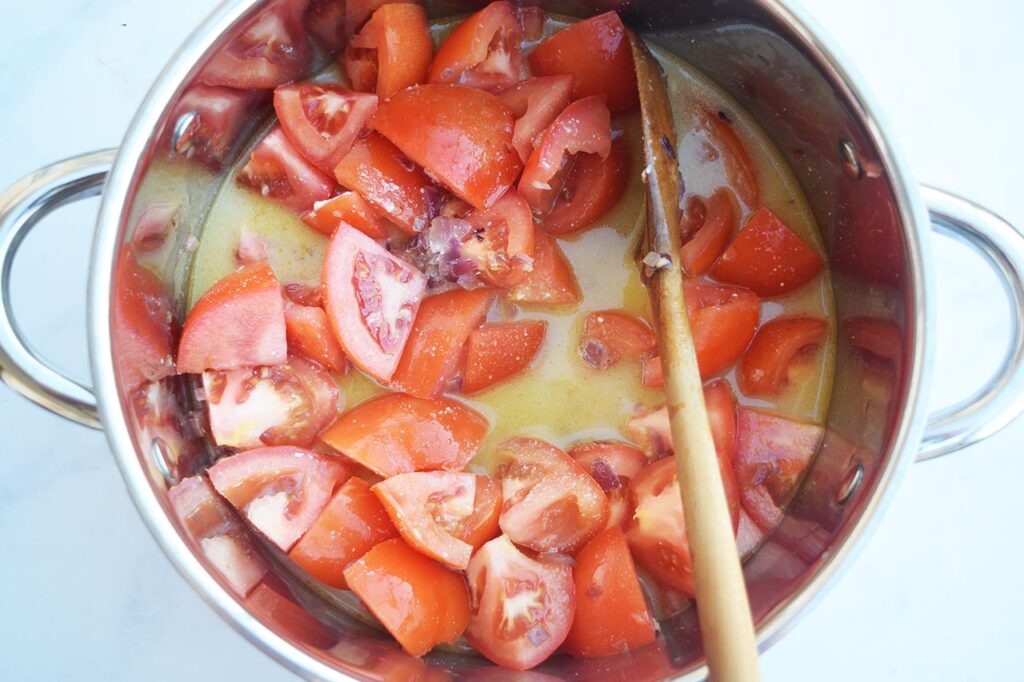 Broth added to tomatoes, onions and garlic in a soup pot.