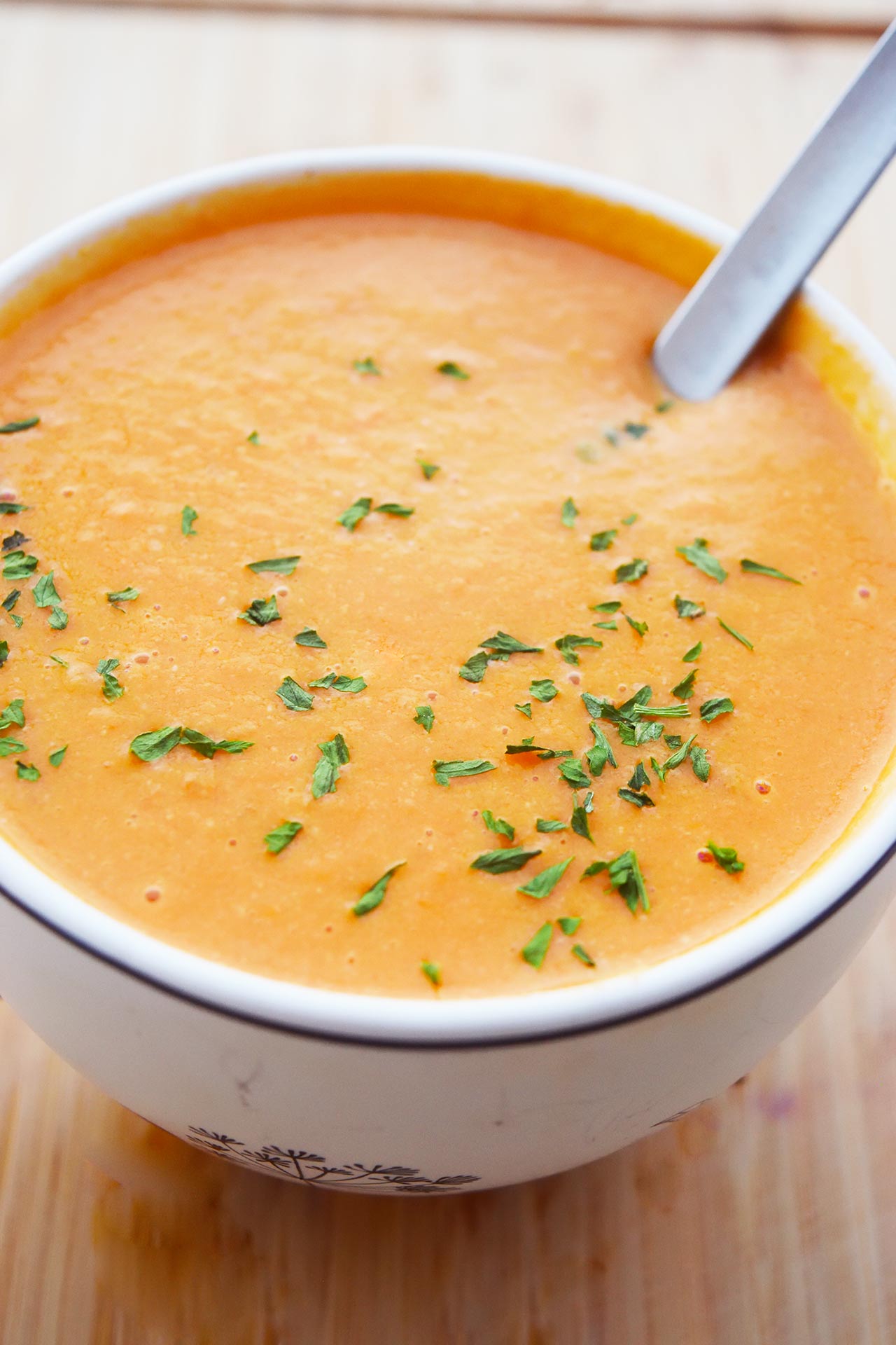 Creamy tomato soup in a white mug with a spoon.