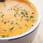 Side view of creamy tomato soup in a white mug with parsley sprinkled over the top.
