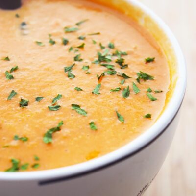 Side view of creamy tomato soup in a white mug with parsley sprinkled over the top.