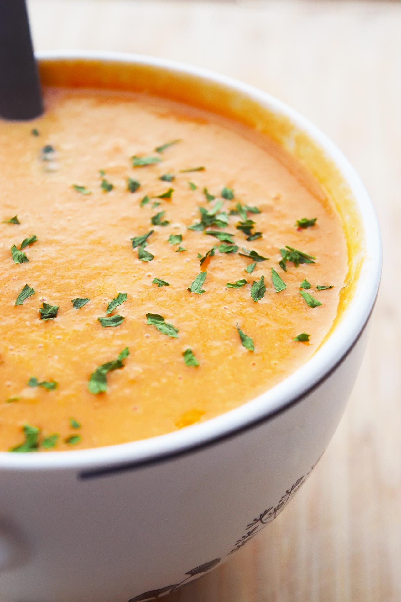 Side view of creamy tomato soup in a white mug with parsley sprinkled over the top.
