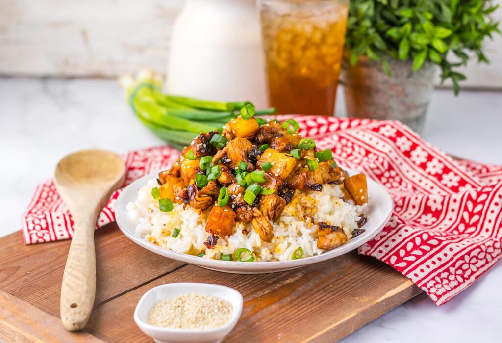 A white bowl holds a pile of Pineapple Chicken served over rice.