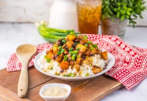 A white bowl holds a pile of Pineapple Chicken served over rice.