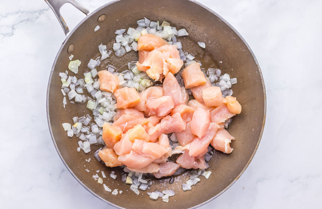 Chicken pieces added to onions in a skillet.