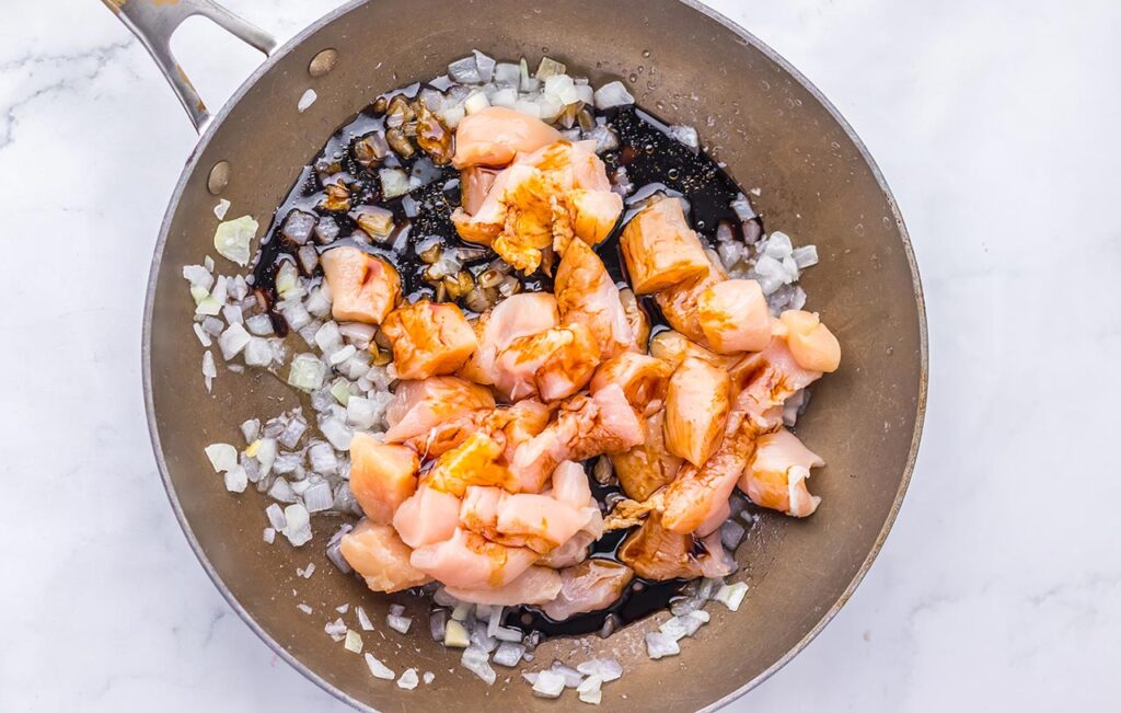 Sauce poured over chicken and onions in a skillet.
