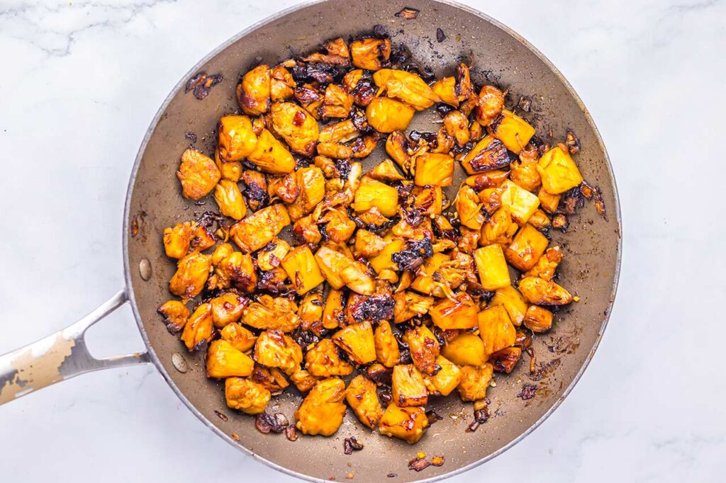 Pineapple chunks added to a skillet of meat, onions, and sauce.