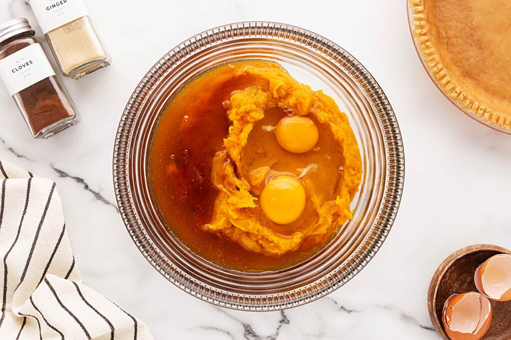 Eggs added to pumpkin puree and honey in a mixing bowl.