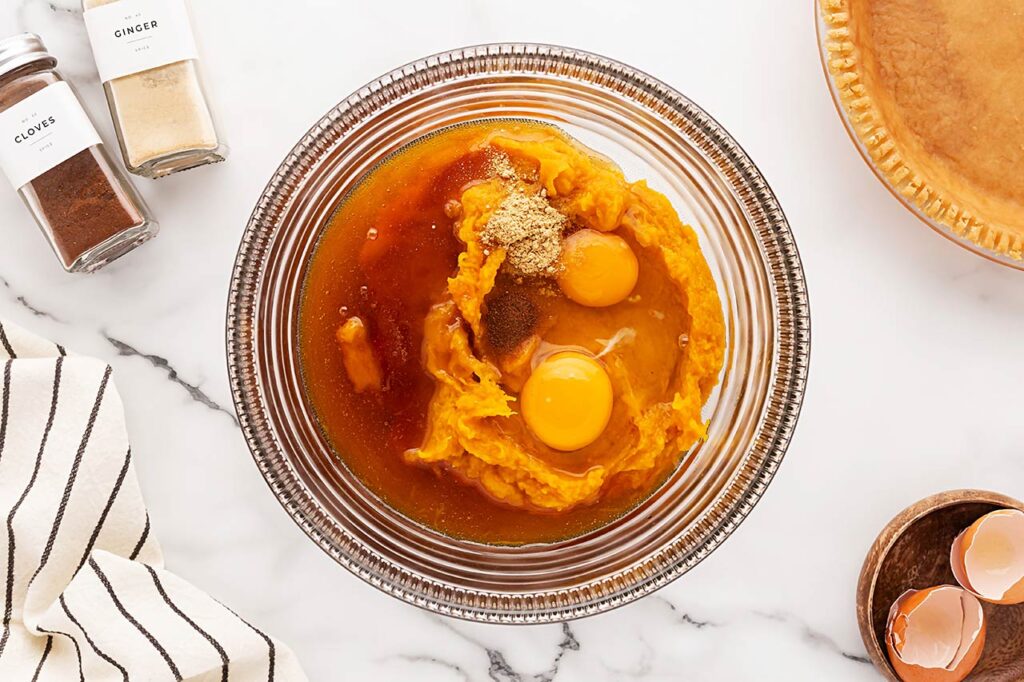 Spices added to pumpkin puree, honey, and eggs in a mixing bowl.