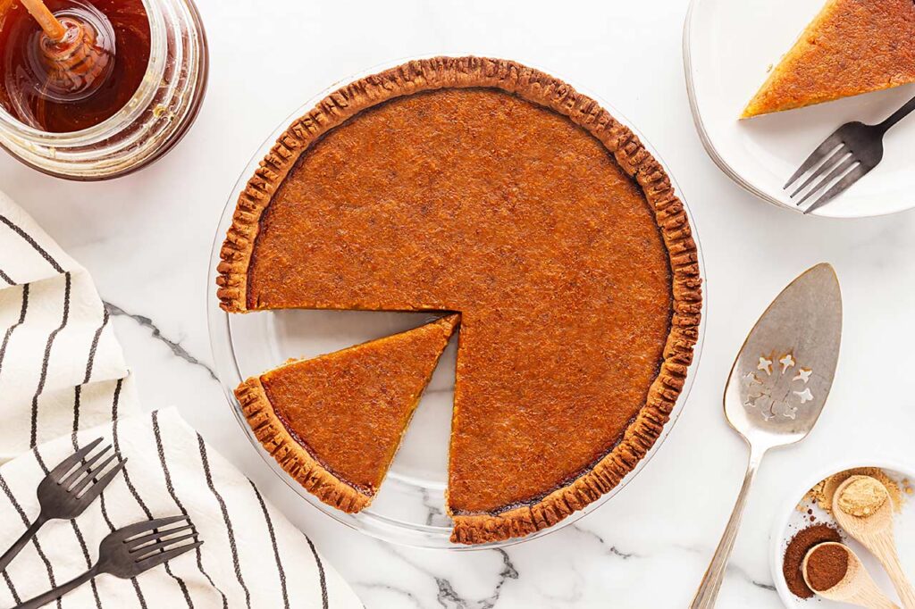 Overhead view of a whole pumpkin pie with a cut piece sitting in the pan.