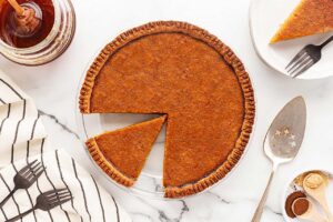 Overhead view of a whole pumpkin pie with a cut piece sitting in the pan.
