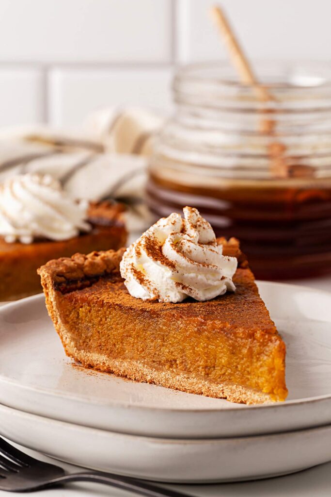 A single slice of pumpkin pie with whipped cream sitting on a plate.