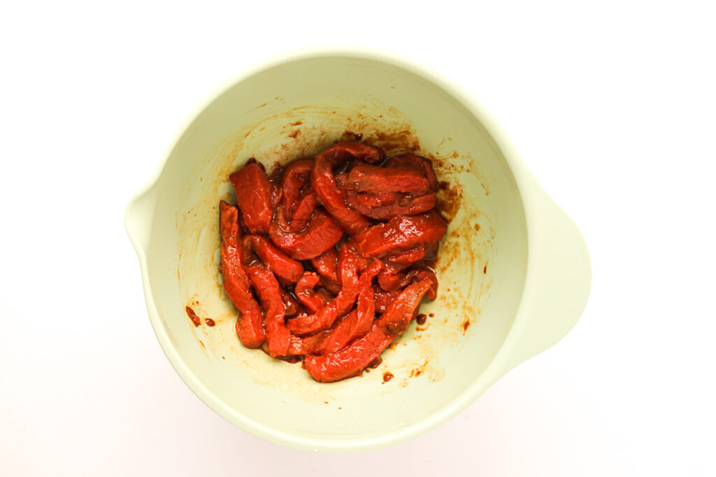 Steak mixed with fajita seasoning in a mixing bowl.