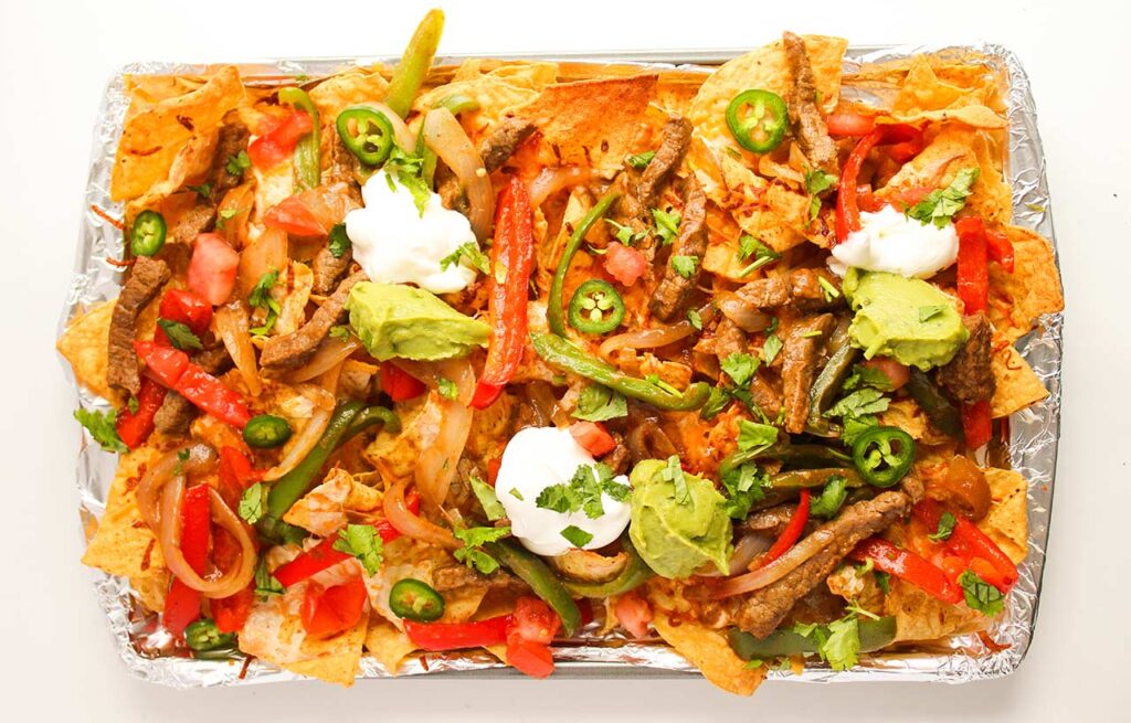 Toppings of sour cream, guacamole, sliced jalapenos, and fresh, chopped cilantro spread over the steak nachos.