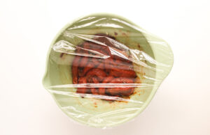 Bowl with steak covered with plastic wrap for marinating.