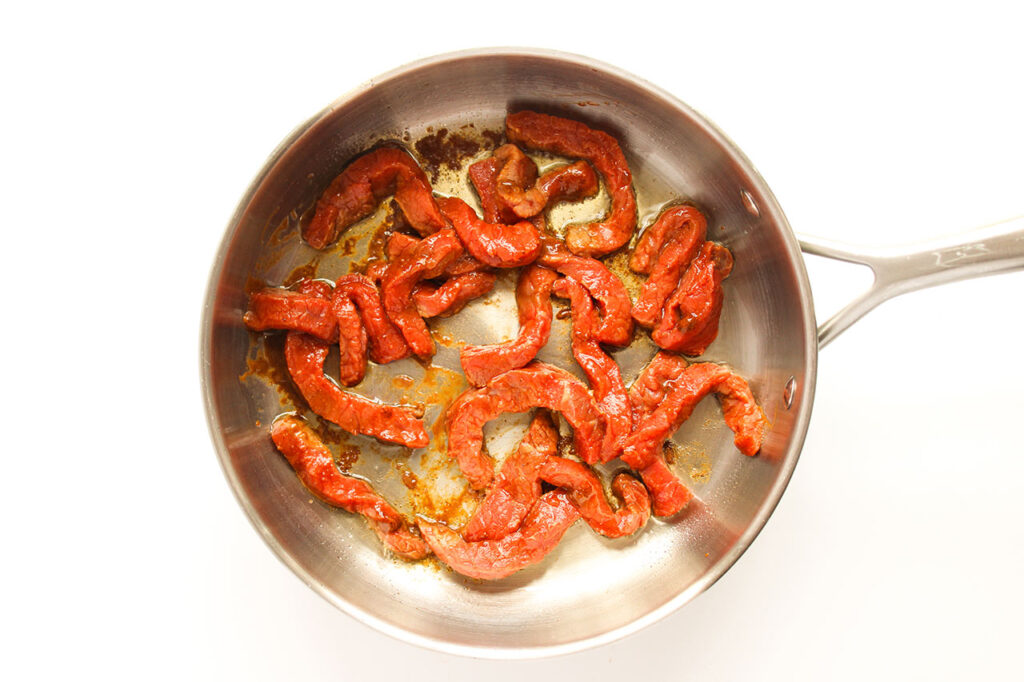 Seasoned steak strips cooking in a skillet.