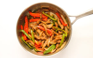 Cooked steak with peppers and onions in a skillet.