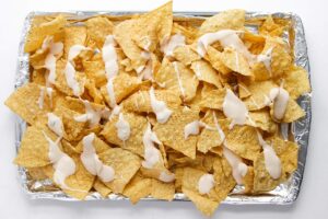 Cheese sauce drizzled over corn chips on a baking pan.