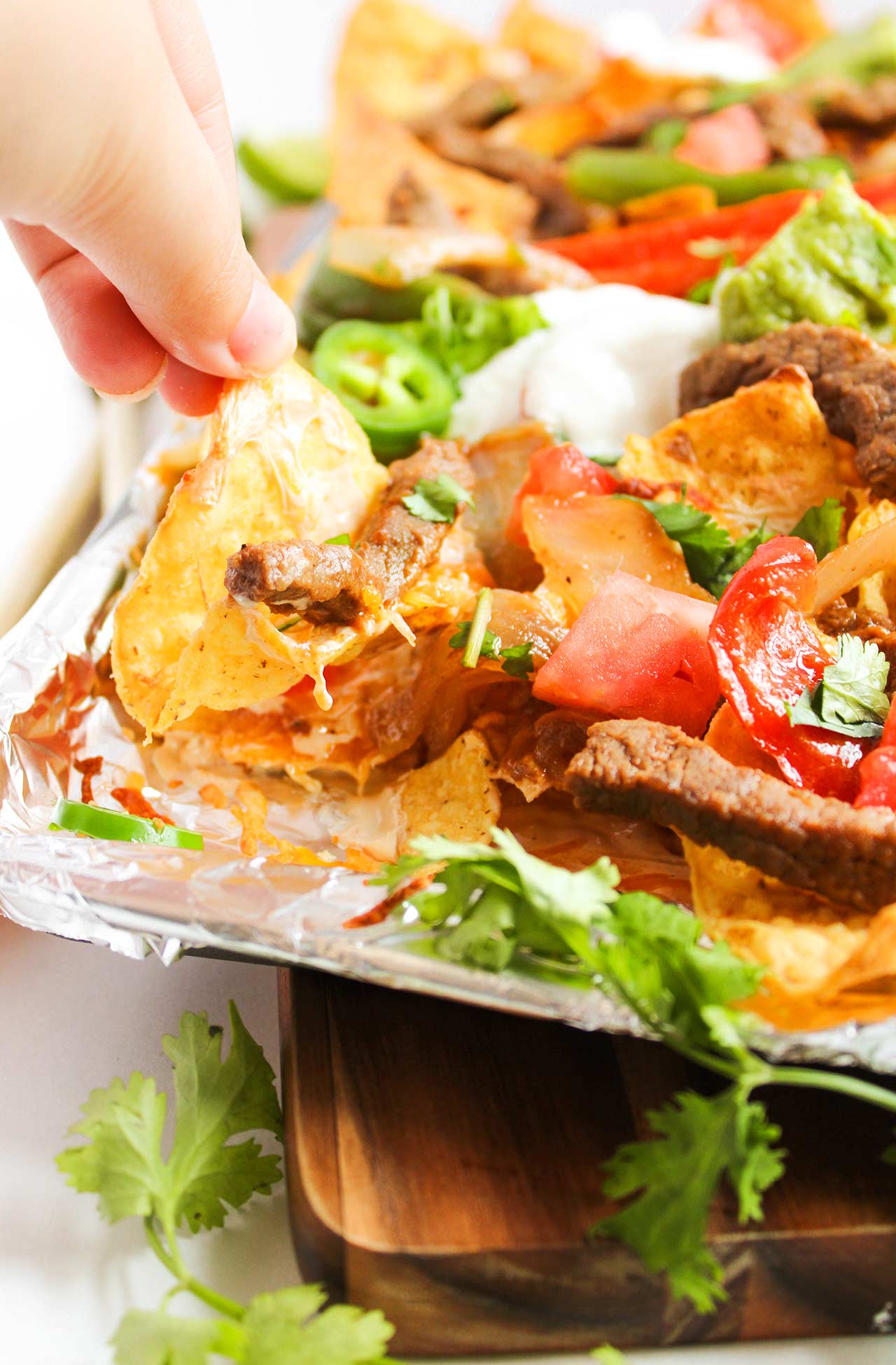A hand reaches for a nacho from a sheet pan full of Steak Nachos.