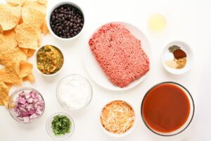 Beef Enchilada Nachos ingredients gathered on a white surface. Overhead focus.