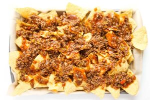 Meat sauce poured over corn chips on a parchment-lined baking sheet.