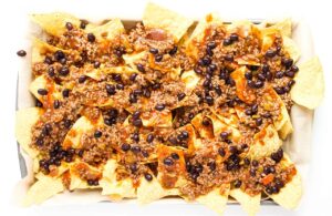Black beans sprinkled over the chips and meat sauce on a baking sheet.
