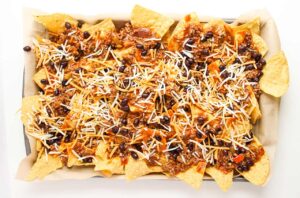 Cheese sprinkled over nachos on a baking sheet.