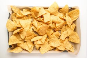 Corn chips spread over a parchment-lined baking pan.