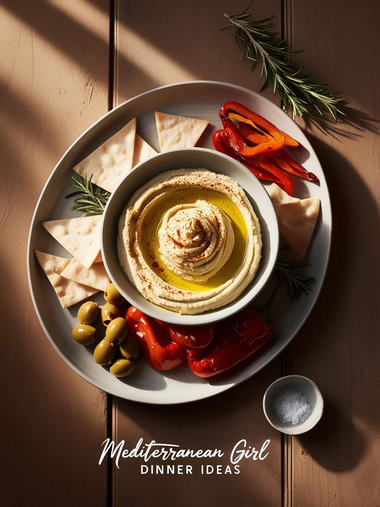 Overhead focus. A plate holds a bowl of hummus with pita chips, olives, and red bell pepper strips.