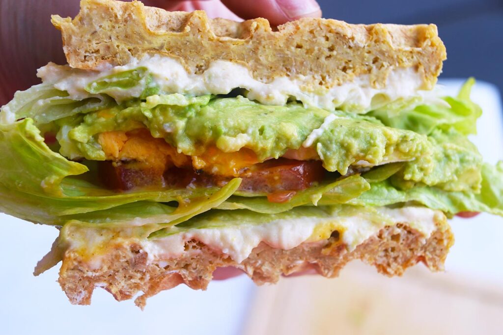 A hand holds half a Breakfast Mediterranean Sandwich showing all it's layers.