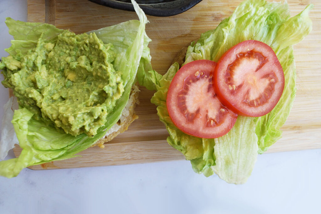 Smashed avocado spread on one piece of bread with tomato slices on the other.