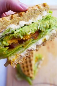 A hand holds half a Breakfast Mediterranean Sandwich over a wood cutting board.